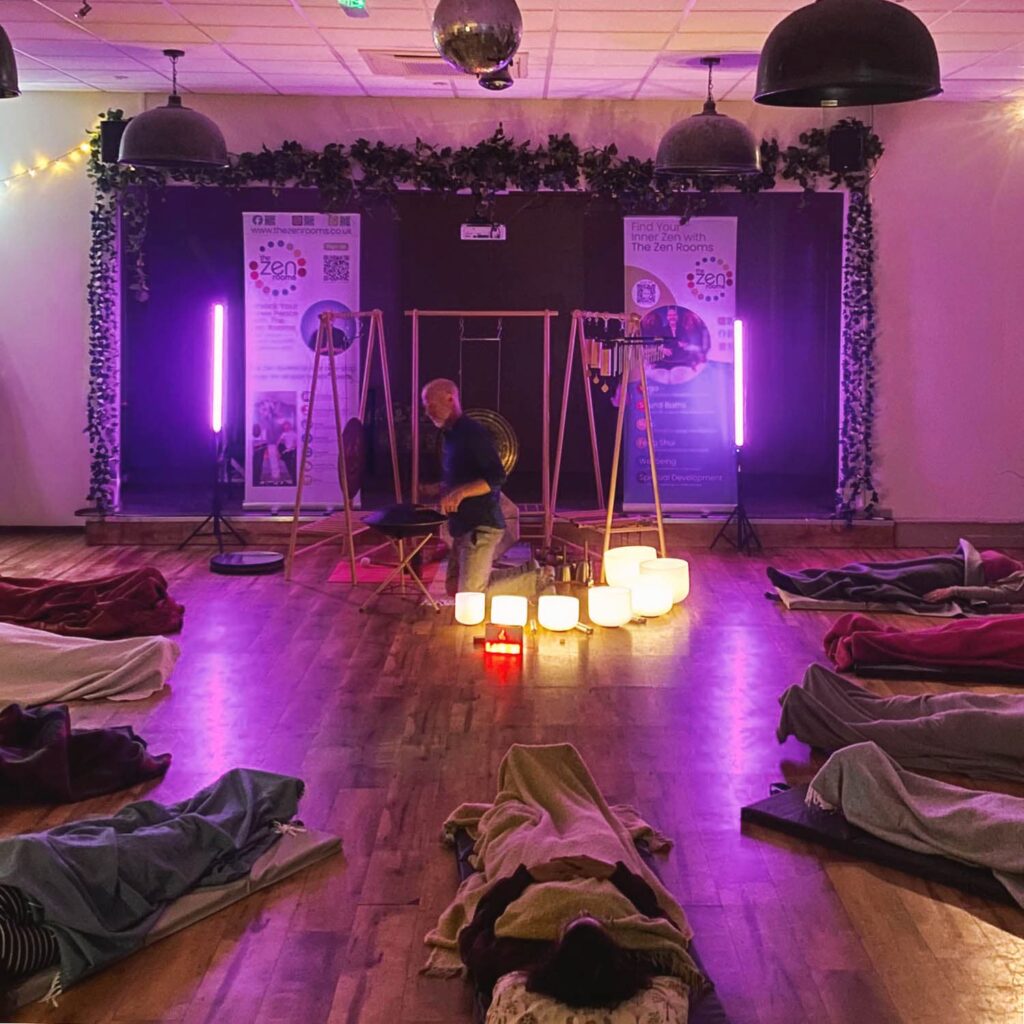 Participants resting on mats during a community sound healing session led by Neil Perry-Timson.